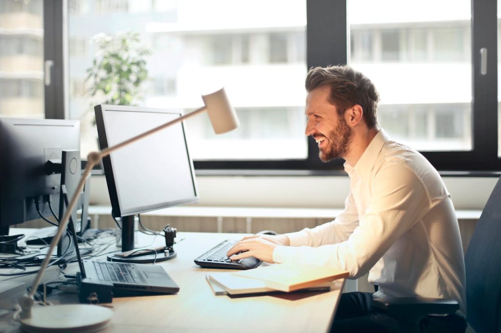 pexels-photo-840996 Man in White Dress Shirt Sitting on Black Rolling Chair While Facing Black Computer Set and Smiling
